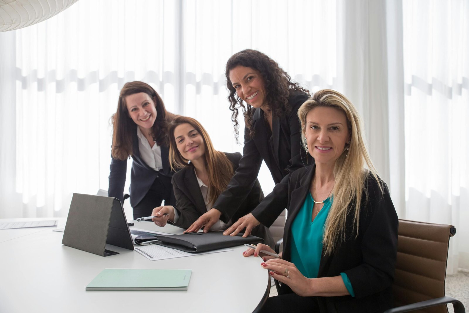 Four businesswomen in a meeting room, collaborating and smiling during a team discussion.